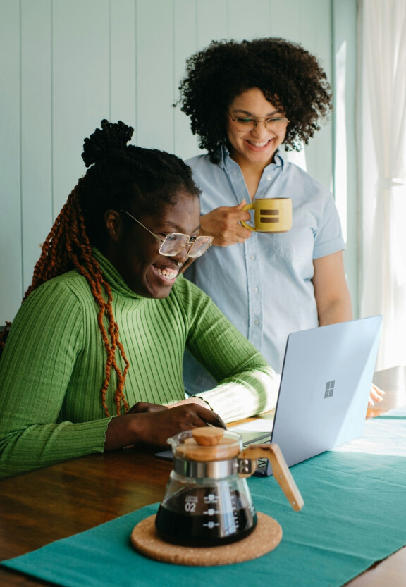 Twee jonge vrouwen, lachend bij een laptop
