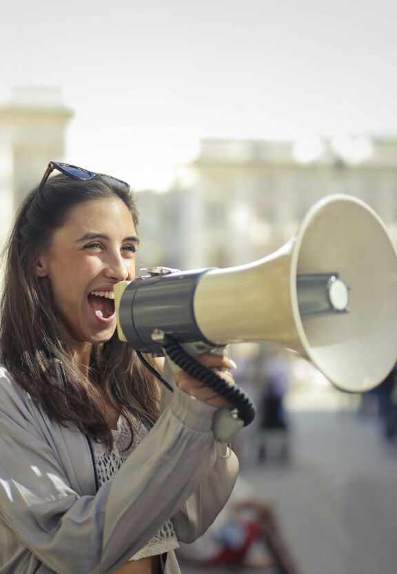 Woman, smiling. Shouting through a megaphone.
