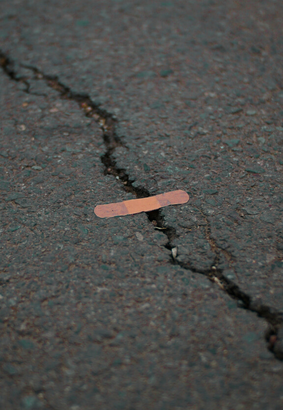 A band-aid over a crack in the asphalt, to illustrate the difficulty of healing.