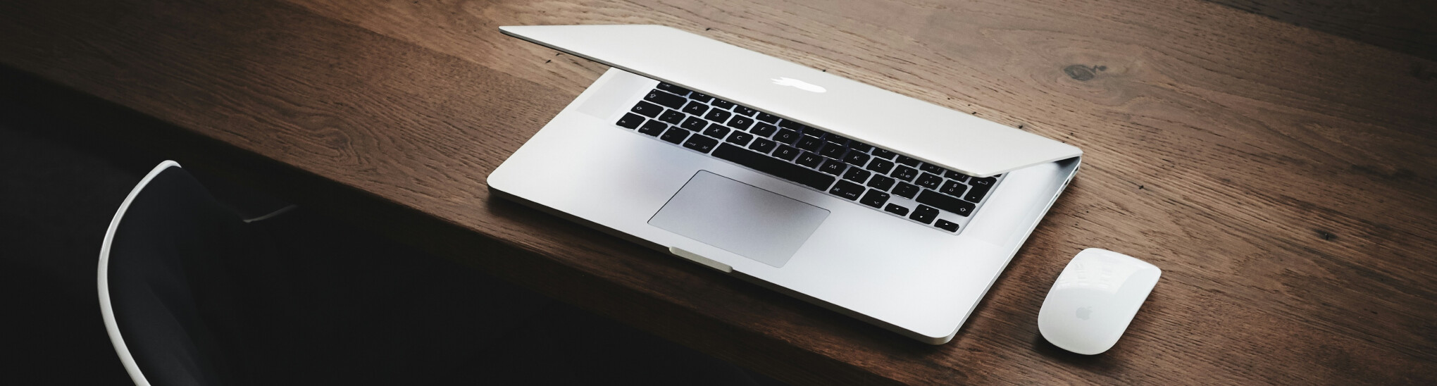 An office chair behind a desk with a macbook and a mouse