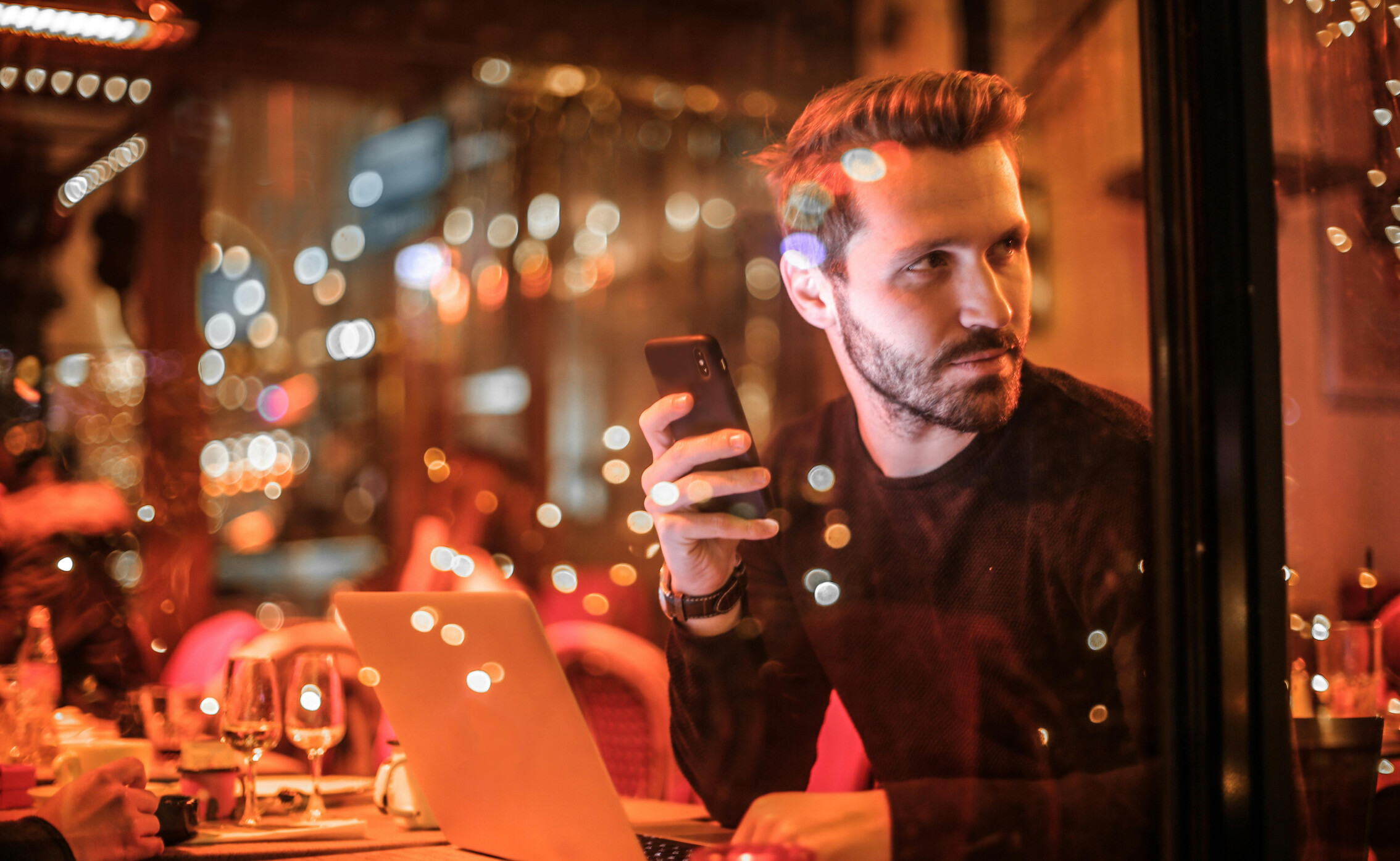 man kijkt vragend om zich heen in restaurant, zit met telefoon en laptop